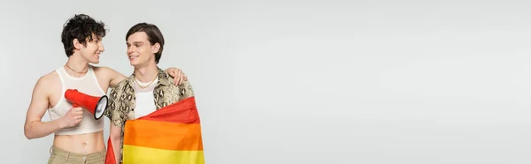 Heureux couple bigender avec haut-parleur et drapeau lgbt se regardant isolés sur gris, bannière — Photo de stock