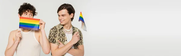 Cheerful pansexual person looking at partner obscuring face with small lgbt flag isolated on grey, banner — Stock Photo
