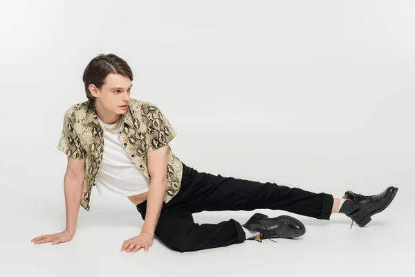 Full length of stylish pansexual person in snakeskin print blouse and black pants posing on grey background — Stock Photo