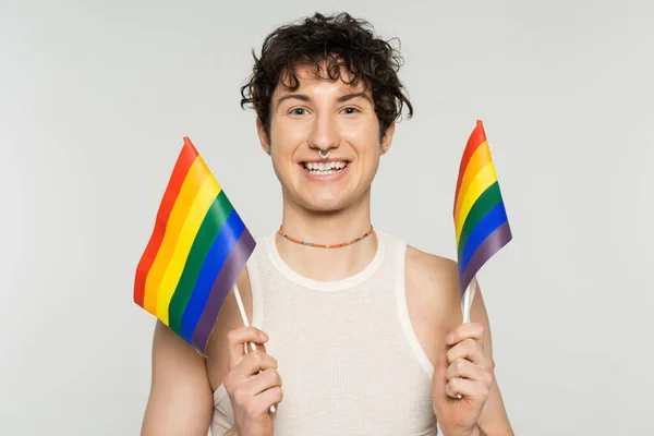Overjoyed nonbinary person in colorful beads holding small lgbt flags isolated on grey — Stock Photo