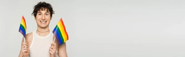 Cheerful bigender person in tank top holding small lgbt flags isolated on grey, banner — Stock Photo