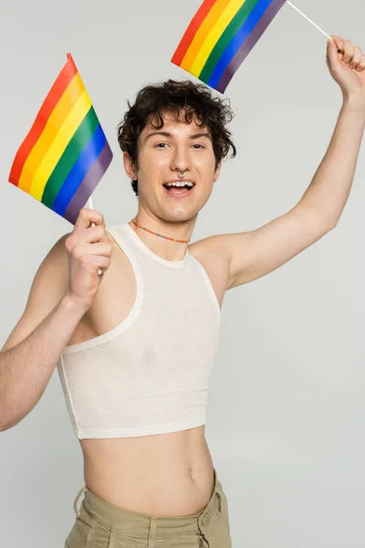 Carefree bigender person in crop top standing with small lgbt flags isolated on grey — Stock Photo