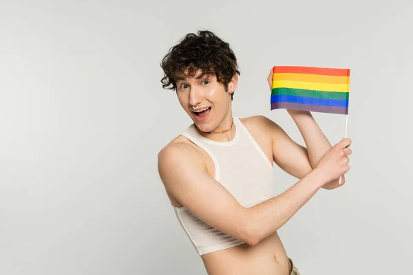 Amazed pangender person showing small lgbt flag at camera isolated on grey — Stock Photo