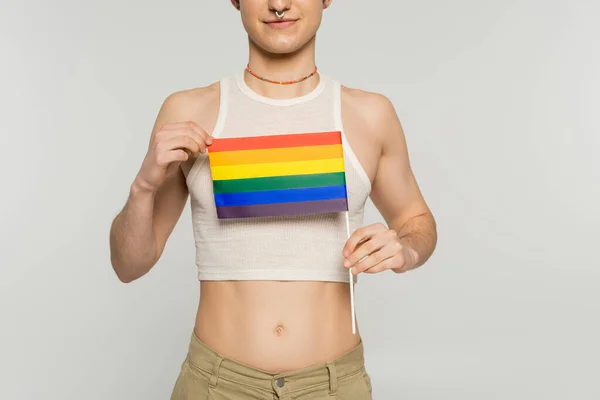 Partial view of young pangender model in crop top holding small lgbt flag isolated on grey — Stock Photo