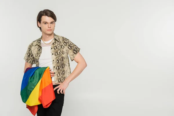 Стильная пансексуальная модель с флагом lgbt, стоящая с рукой на бедре и смотрящая на камеру, изолированную на сером — стоковое фото