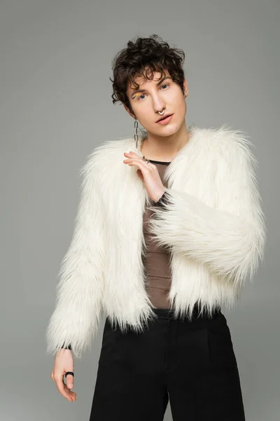 Fashionable nonbinary person in white faux fur jacket looking at camera isolated on grey — Stock Photo