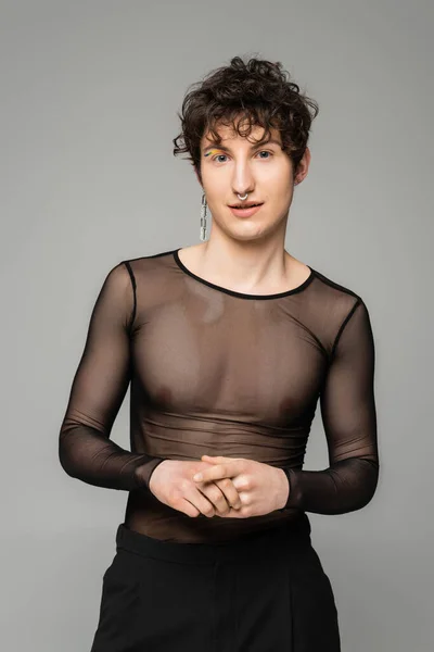 Positiver pansexueller Mensch in schwarzem transparentem Oberteil und silbernem Ohrring, der auf grau isoliert in die Kamera blickt — Stockfoto
