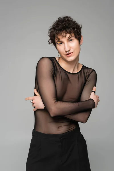 Brunette pansexual model in black transparent top posing with crossed arms isolated on grey — Stock Photo