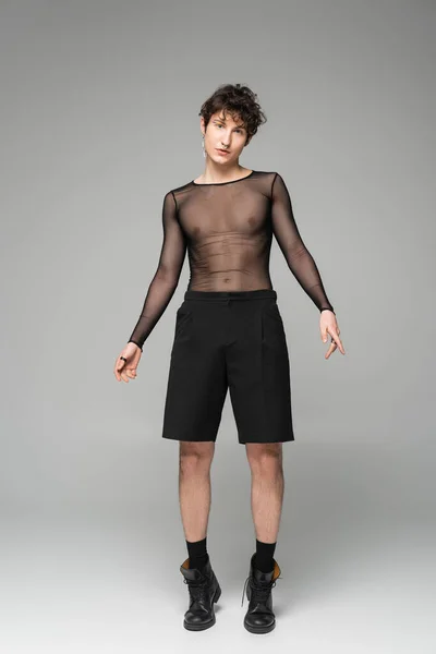 Full length of nonbinary person in transparent top and black shorts on grey background — Stock Photo