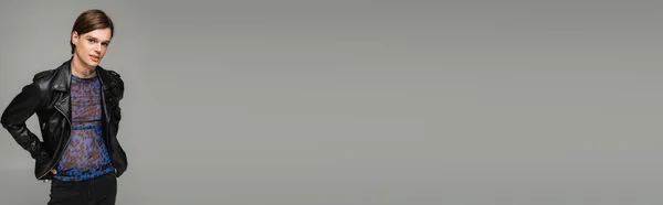 Jeune personne non binaire en veste en cuir noir et imprimé animal haut regardant la caméra isolée sur gris, bannière — Photo de stock
