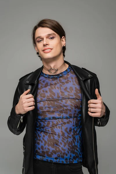 Joyful pansexual model in animal print top and black leather jacket smiling at camera isolated on grey — Stock Photo