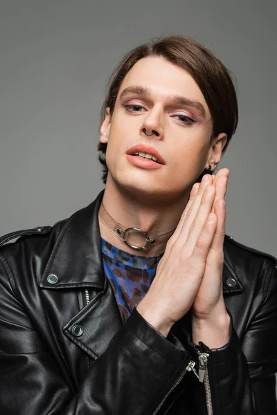 Portrait of stylish pansexual person with makeup and praying hands looking at camera isolated on grey — Stock Photo