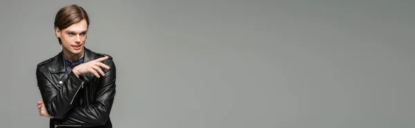 Persona pansessuale sorridente in giacca di pelle nera distogliendo lo sguardo e indicando con dito isolato su grigio, banner — Foto stock