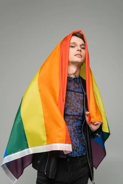 Trendige Pangender-Person, die sich mit Regenbogenfahne verhüllt und isoliert auf grau in die Kamera blickt — Stockfoto