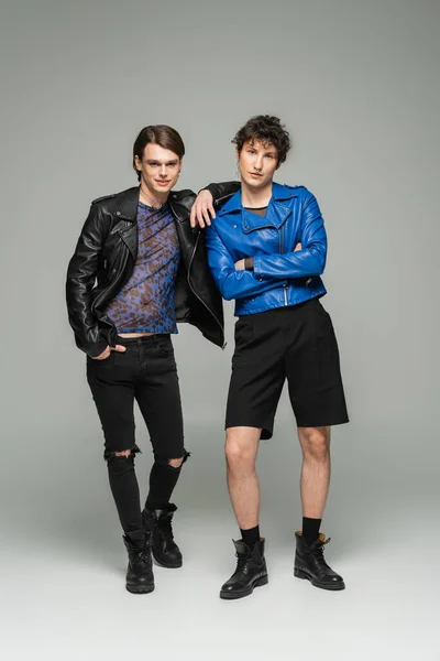 Comprimento total de elegante casal não binário em jaquetas de couro e botas de pé sobre fundo cinza — Fotografia de Stock