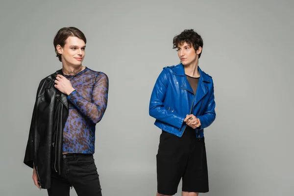 Junge nichtbinäre Person in blauer Lederjacke, die ihren modischen Partner isoliert auf grau betrachtet — Stockfoto