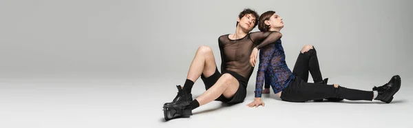 Junge Pangender-Models in stilvoller Kleidung sitzen auf grauem Hintergrund, Banner — Stockfoto
