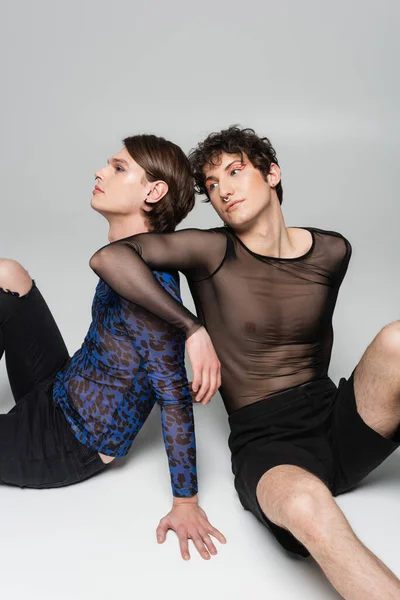 Jovens parceiros pangender em roupas da moda sentado em fundo cinza — Fotografia de Stock