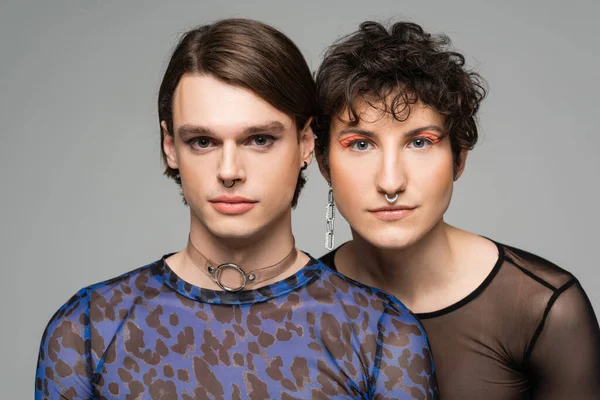 Porträt eines jungen und stilvollen pansexuellen Paares mit Make-up, das isoliert auf grau in die Kamera blickt — Stockfoto