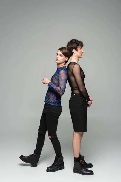Piena lunghezza di partner pansessuali in abiti alla moda in piedi back to back su sfondo grigio — Foto stock