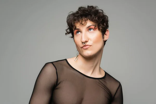 Trendige und verträumte Pangender-Person mit Make-up, die isoliert auf grau schaut — Stockfoto