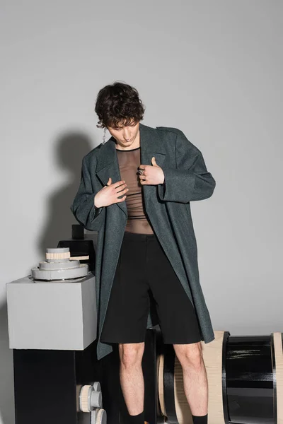 Bruna pansessuale persona in cappotto e pantaloncini neri in piedi vicino al modello di fotocamera fotografica su sfondo grigio — Foto stock
