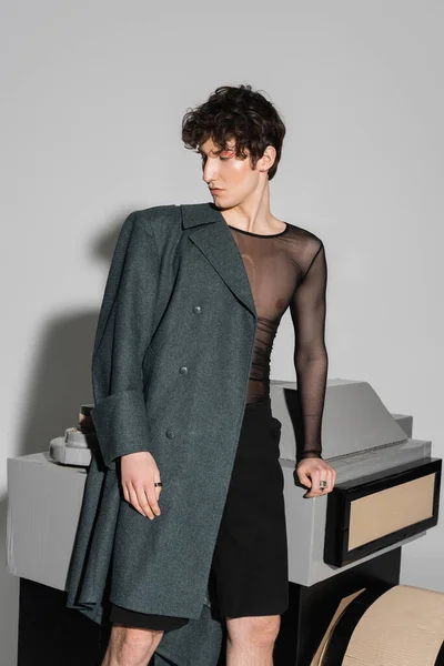 Stilvolle Pangender-Person im Mantel, die in der Nähe des Fotokameramodells auf grauem Hintergrund steht — Stockfoto