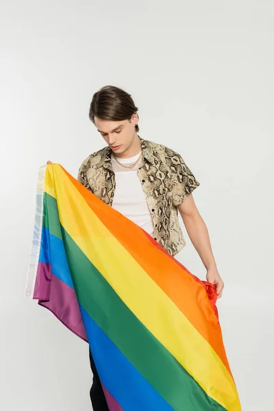 Jeune modèle non binaire en chemisier imprimé animal tenant le drapeau arc-en-ciel isolé sur gris — Photo de stock
