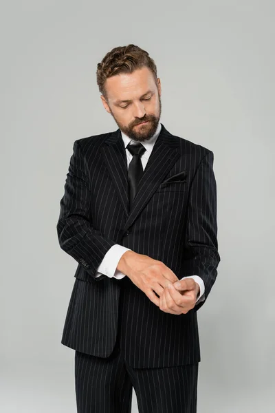 Confident and bearded businessman in formal wear adjusting sleeve isolated on grey — Stock Photo