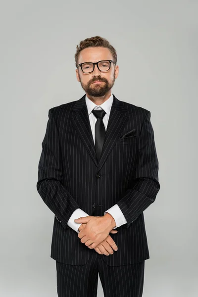 Уверенный и бородатый бизнесмен в формальной одежде и очках, глядя на камеру, изолированную на сером — стоковое фото