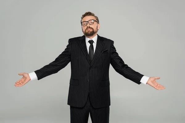 Плутаний бізнесмен у формальному одязі та окулярах, дивлячись на камеру, показуючи жест згинання ізольований на сірому — стокове фото