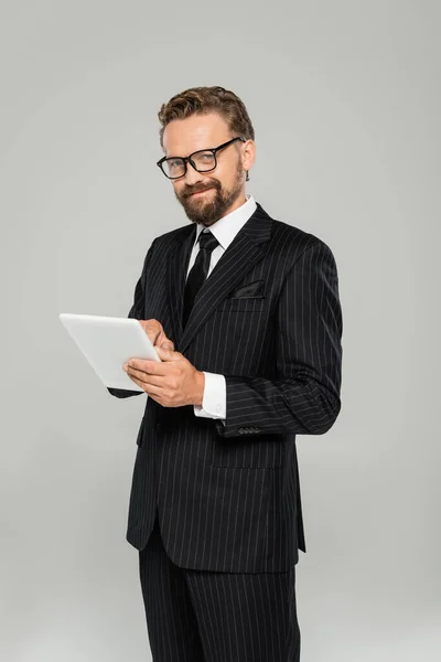 Hombre de negocios feliz en ropa formal y gafas usando tableta digital aislada en gris - foto de stock