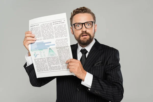 Empresário chocado em terno e óculos segurando jornal isolado em cinza — Fotografia de Stock