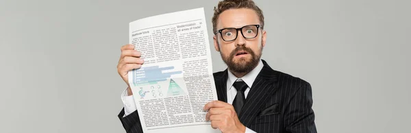 Shocked businessman in suit and glasses holding newspaper isolated on grey, banner — Stock Photo