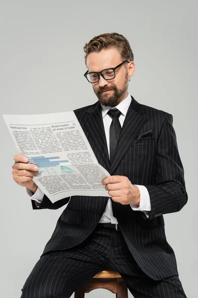 Heureux homme d'affaires en costume et lunettes lecture journal isolé sur gris — Photo de stock
