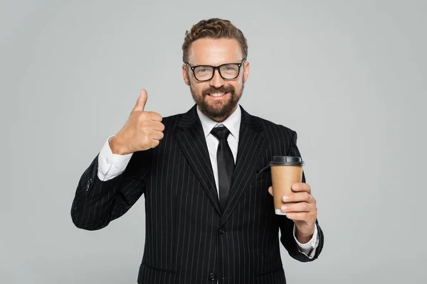 Glücklicher Geschäftsmann in Brille und Anzug, Pappbecher in der Hand und Daumen hoch auf grau — Stockfoto