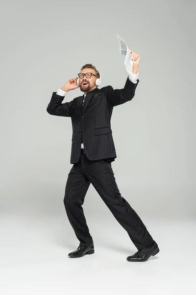 Geschäftsmann mit Brille, der Musik hört und singt, während er Kopfhörer auf grau hält — Stockfoto