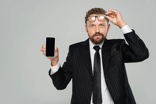 Businessman in suit and glasses showing smartphone with blank screen isolated on grey — Stock Photo