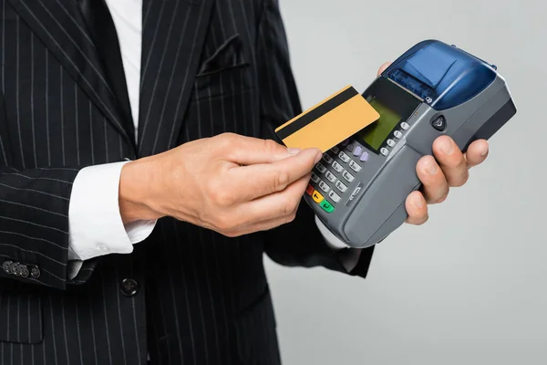 Обрізаний вид бізнесмена в костюмі, що тримає кредитну картку біля платіжного терміналу ізольовано на сірому — стокове фото