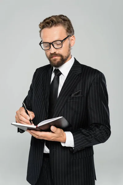 Hombre de negocios bien vestido en gafas y escritura formal en cuaderno aislado en gris - foto de stock