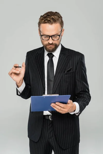 Хорошо одетый бизнесмен в очках и формальной одежды держащий планшет с ручкой, изолированной на сером — Stock Photo