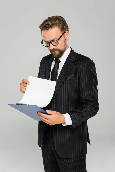 Uomo d'affari ben vestito in occhiali che tiene appunti e carta isolata su grigio — Foto stock