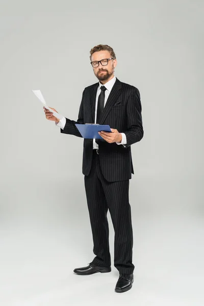Повна довжина добре одягненого бізнесмена в окуляри, що тримає кишеню і папір на сірому — стокове фото