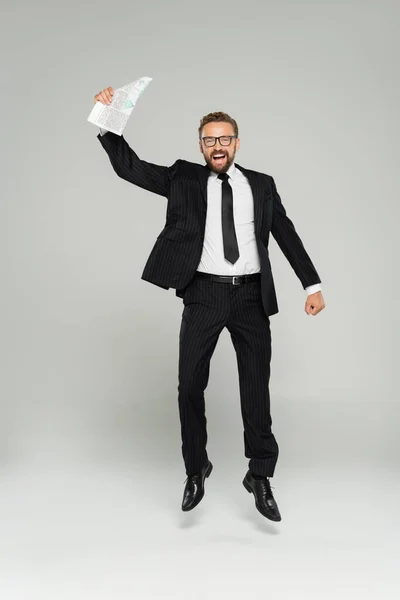 Повна довжина збудженого бізнесмена в окулярах тримає газету, стрибаючи на сірому — стокове фото