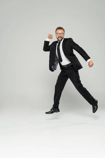 Повна довжина збудженого бізнесмена в окулярах і костюм стрибає на сірому — стокове фото