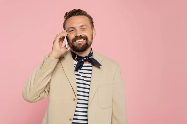 Hombre francés feliz en chaqueta y cuello bufanda hablando en el teléfono inteligente aislado en rosa - foto de stock
