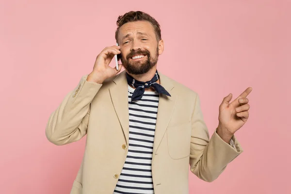 Homem francês alegre em blazer e cachecol pescoço falando no smartphone, apontando para longe isolado em rosa — Fotografia de Stock