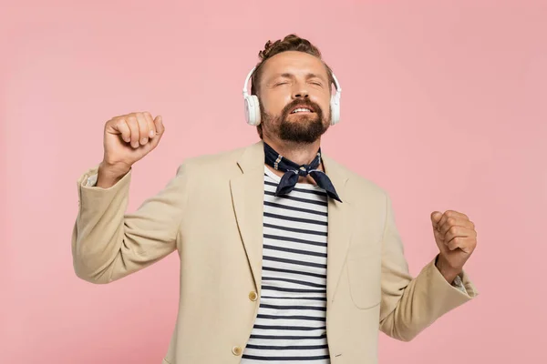 Hombre francés en chaqueta y cuello bufanda escuchar música en auriculares inalámbricos aislados en rosa - foto de stock