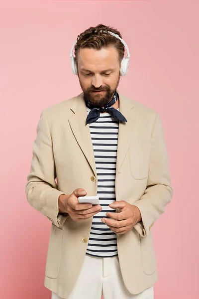 Bearded french man in wireless headphones using smartphone isolated on pink — Stock Photo