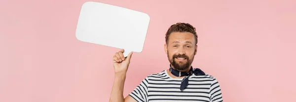 Happy french guy in striped t-shirt and neck scarf holding speech bubble isolated on pink, banner — Stock Photo
